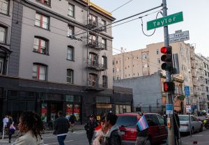 街道路口的Taylor与Gene Compton’s Cafeteria Way路牌,周围有建筑、车辆和行人